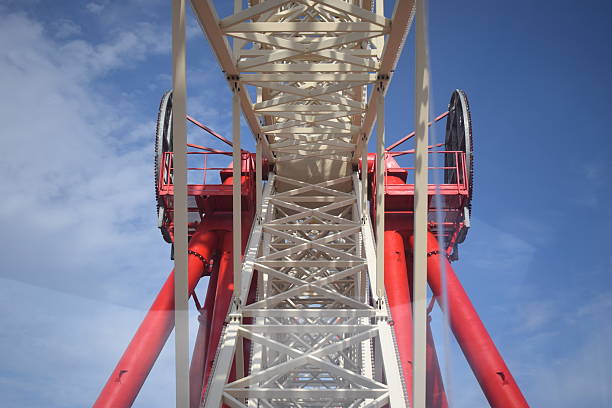 Ferris wheel construction seen from one of the cabins. Part of a white metal construction of the attraction. Ferris wheel inner construction against the blue sky with white clouds