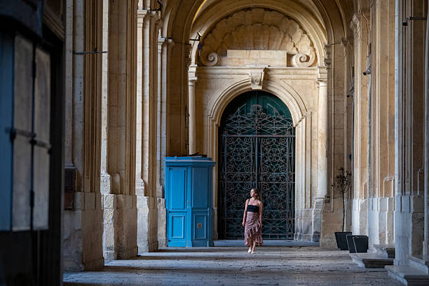 Woman walks under ancient stone archways, Valetta