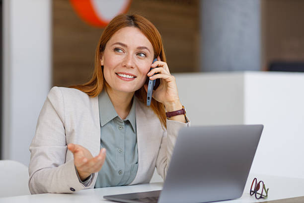 istock Smiling professional communicating via smartphone while typing on laptop in contemporary workspace 2218317798