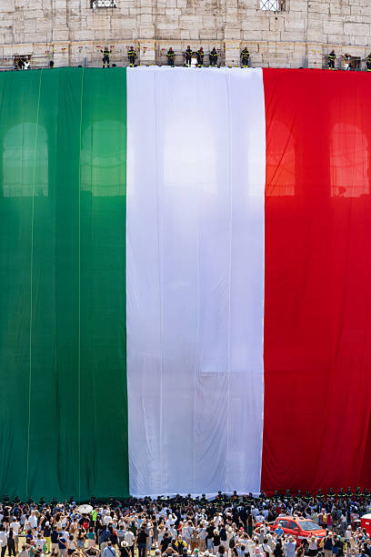 Rome, Italy - June 2, 2025:  Large group of people gathered by Coliseum to celebrate Republic day. Enormous Italian flag managed by firefighters hanging on the Coliseum wall.