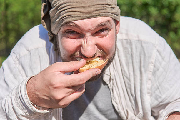 Playful portrait of a young man outdoors looking at the camera while eagerly eating his breakfast, biting into a slice of toast with egg.