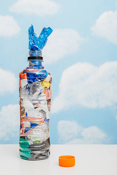 istock Plastic bottle filled with compressed plastic waste and piece of wrapper standing out from the bottle's mouth. 2218321249