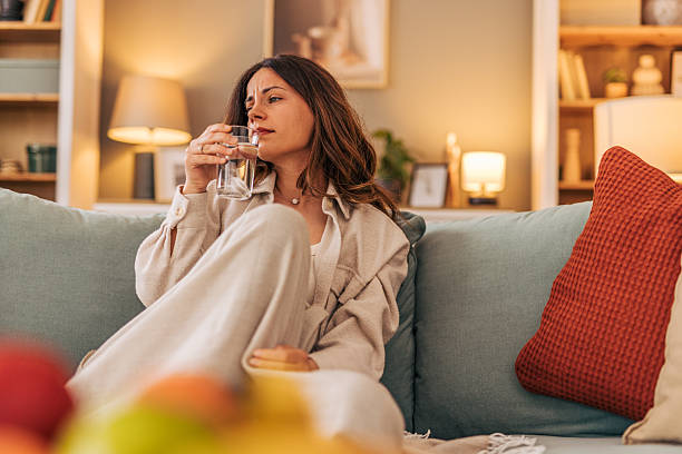 istock Sick young woman drinking water on sofa at home 2218322543