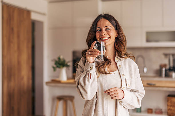 istock Young woman drinking water in modern kitchen, smiling at camera 2218322857