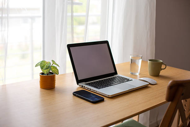 Bright home office setup with laptop, smartphone, and potted plant on a wooden desk, ideal for remote work or studying