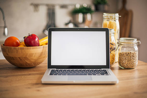 Laptop with blank screen in a modern kitchen with fruits and grains, perfect for displaying cooking websites or recipes