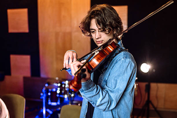 Portrait with stunning, young musicians, violinist wearing elegant suit and eyeglasses holding musical instrument and smiling over blue background. Concept of music, art, hobby, human emotions, ad