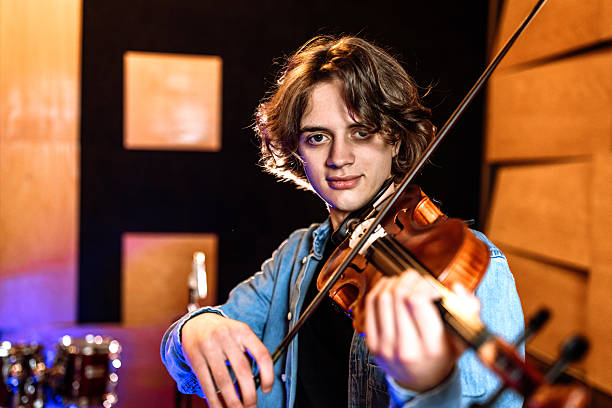 Young male violinist practicing playing violine while looking at camera.