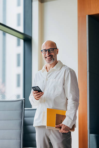 Smiling Businessman Holds Documents and Smartphone in Modern Office Setting
