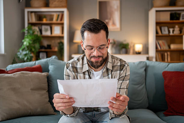 istock Smiling man reading a letter at home on the sofa 2218337351