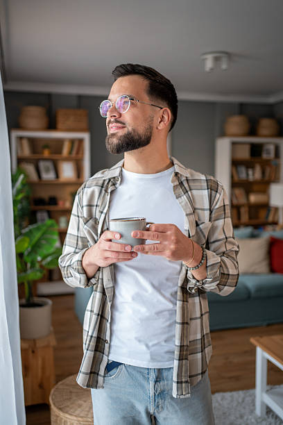 istock Young man drinking coffee and looking out the window at home 2218338139
