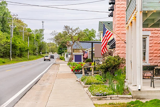 Two flags fly in front of local shops next to the road in Marblehead Ohio. The outside of the stores are well landscaped with Spring flowers in bloom.  The buildings are reminiscent of days gone by.