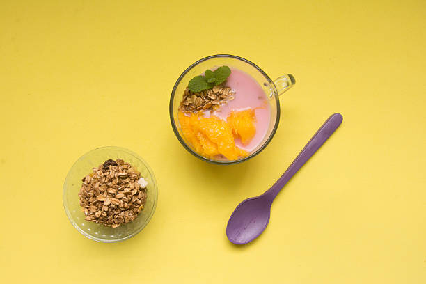 Yogurt with mango and granola in glass on yellow background