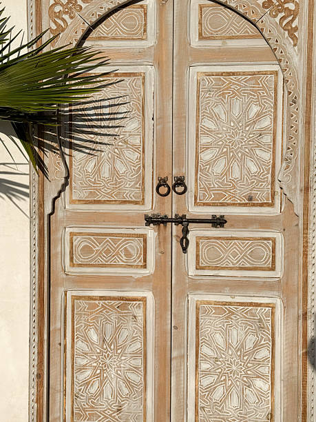 Traditional Moroccan Style carved wood door with decorative white washed boho pattern made in Marrakech medina souq with palm leave in sunlight