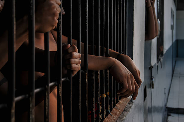 istock prisoner's hands behind bars with black background 2218350221