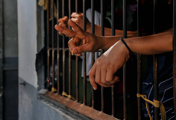 istock prisoner's hands behind bars with black background 2218350222