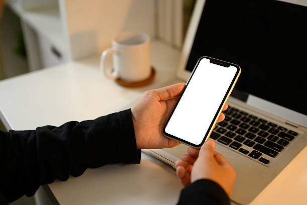 istock Hands holding a modern smartphone with blank screen in front of a laptop 2218352086