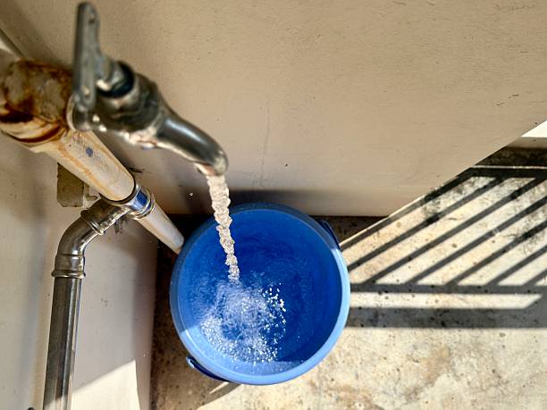 Overhead view of water valve tap filling water into plastic blue bucket, aka pail or barrel