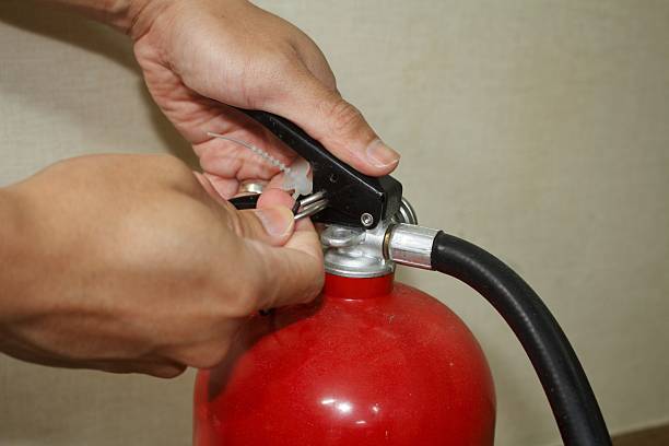 istock Hands pulling the safety pin from a red fire extinguisher. 2218358597