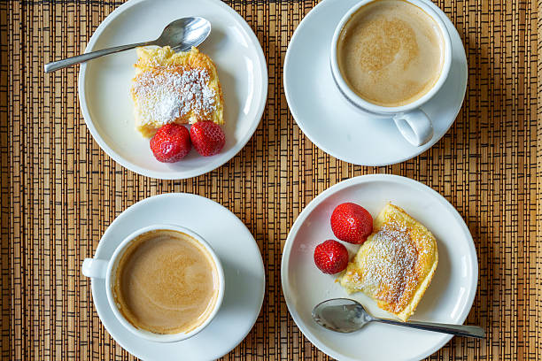 A coffee table is set with two sets of coffee and cake. Semolina slices sprinkled with powdered sugar and strawberries for coffee.