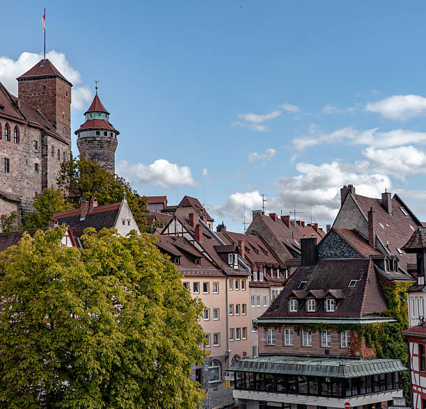 This high-resolution image captures the historic architecture of Nuremberg's old town, featuring red-tiled rooftops, half-timbered facades, and ivy-covered buildings. A perfect representation of traditional Bavarian design and European urban charm, this scene showcases the layered rooftops, textured walls, and a lively pedestrian area below. Ideal for travel, architecture, culture, or heritage-related editorial and commercial uses.
