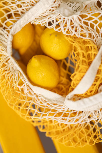 High angle shot of lemons in mesh bag on yellow bench without people