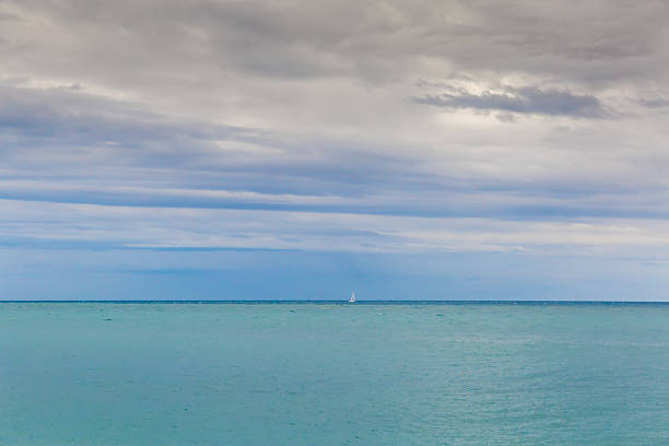 Part of the sea with water surface roughness and distant white sailing yacht on a horizon against the cloudy sky in overcast day