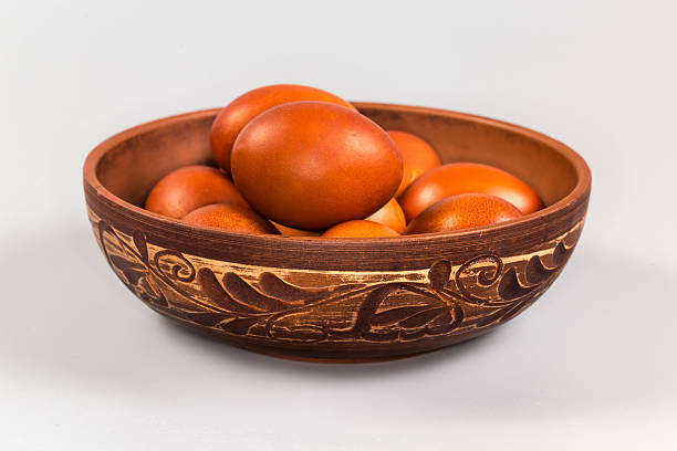 Several Easter eggs painted brown in a clay bowl decorated with plant pattern on a gray background, front view close-up in selective focus