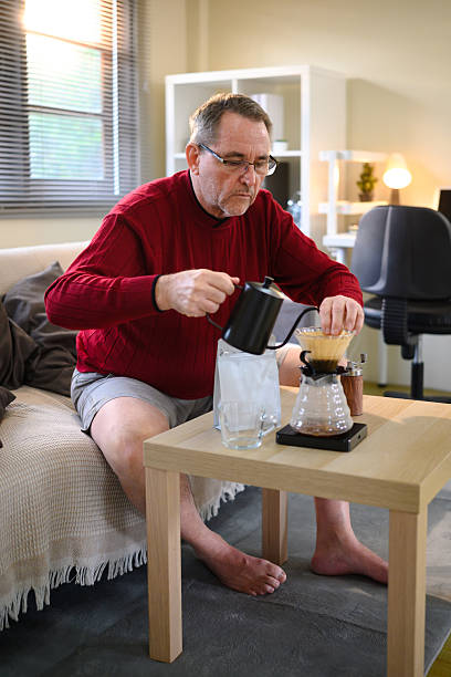 Elderly man making fresh coffee with manual brewing setup in a living room