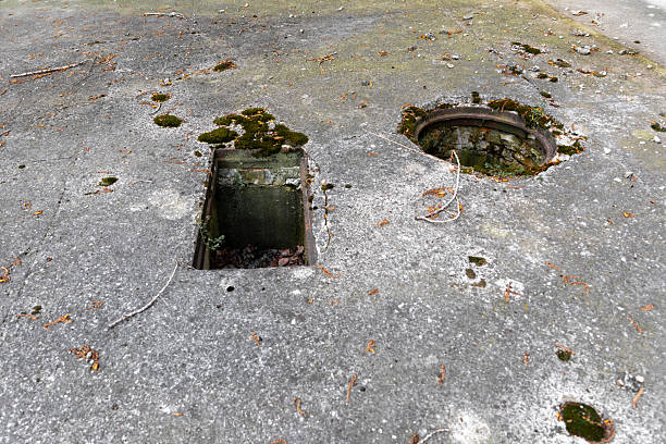 istock Weathered concrete ground with two open, moss-covered holes, surrounded by debris and signs of decay in an abandoned industrial or military area. 2218388321