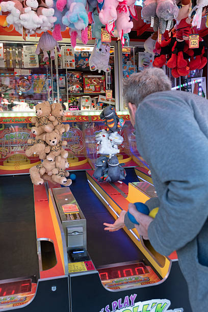 A man rolls colourful balls during a classic skeeball-style arcade game at a Dutch funfair. Soft toy prizes and boxed games fill the booth, creating a nostalgic and competitive carnival atmosphere.