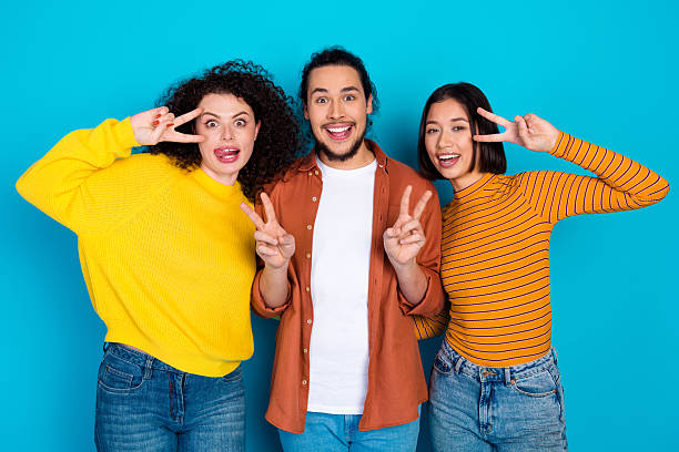 Three teenagers wearing funny Christmas clothes, holding presents and bauble laughing at the camera. Studio shot against green background.