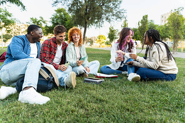 istock Friends sitting on the grass on campus, laughing using cell mobile phones sharing on social media 2218397572