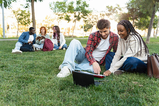 istock African American girl and caucasian young students learning together, reading, looking at notes and a laptop on the university campus park 2218397743