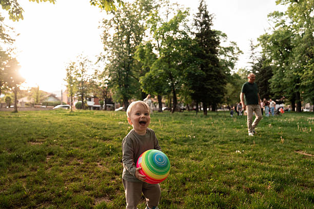 Joyful toddler running through the park holding a colorful ball. Energetic playtime and carefree childhood moment.