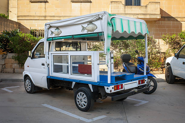 Zabbar, Malta- 06/01/2025: Small fish delivery truck with a striped awning and fish signs, parked in a Maltese town. Traditional street vendor vehicle for selling fresh seafood.