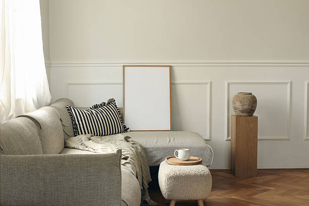 istock Empty wooden picture frame on grey sofa, striped pillow. White stucco panelled wall. Minimal elegant poster mockup. Artistic template. Cup of coffee. Wooden pedestal, clay vase. Scandinavian interior 2218405833