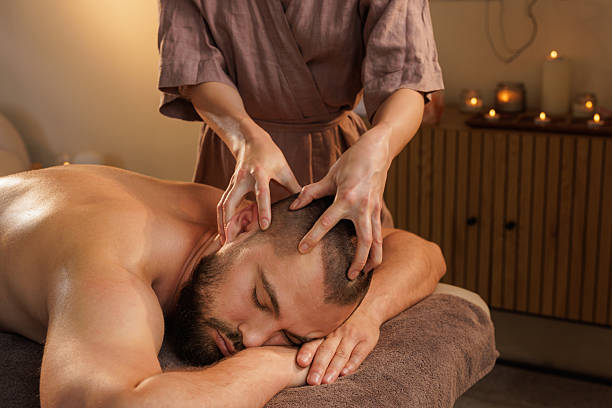 istock Professional therapist performing a relaxing head massage on a bearded man lying on a spa table in a calm, candle-lit wellness room with warm and peaceful atmosphere. 2218406793
