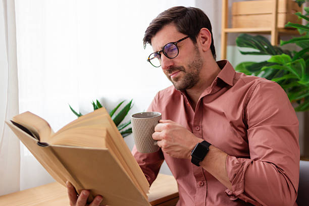 istock Focused man reading book and drinking coffee at home 2218409798