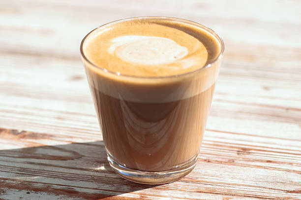 istock Glass of flat white coffee on a rustic wooden table in sunlight 2218411233