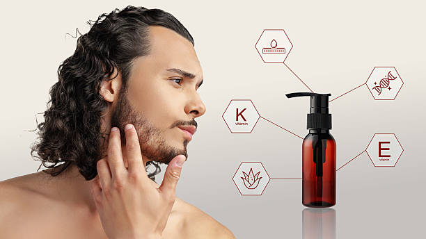 A man with wavy, dark hair gently touches his beard while showcasing an oil bottle enriched with vitamins K and E. The backdrop emphasizes the product benefits.