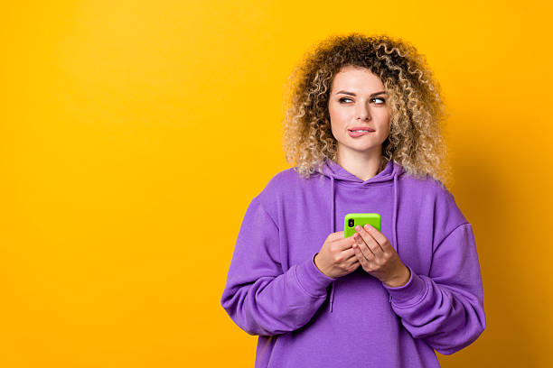 istock Photo of young lady look empty space hold mobile guess look empty space think isolated over yellow color background 2218415789