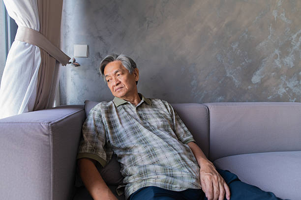 Homem asiático chinês idoso deitado no sofá de casa com uma emoção triste, foto de stock Homem asiático chinês idoso deitado no sofá de casa sozinho, fotos de homem velho com rugas, fotos e imagens royalty-free