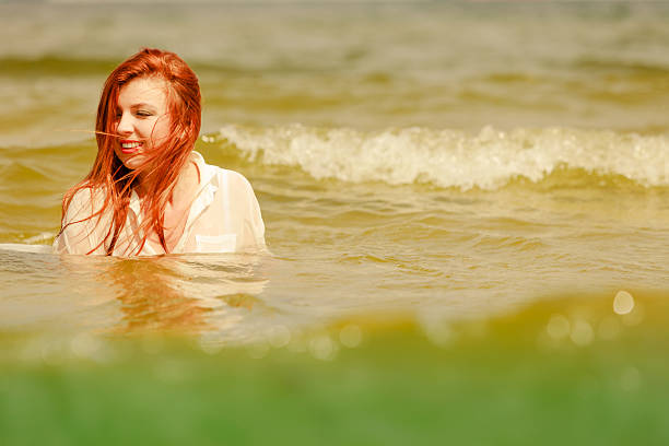 Summer fun, recreation outside concept. Redhead adult woman playing in water during summertime, having great time and smiling joyfully