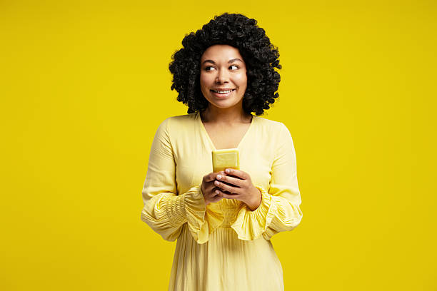istock Young woman using smartphone and looking away smiling on yellow background 2218423393