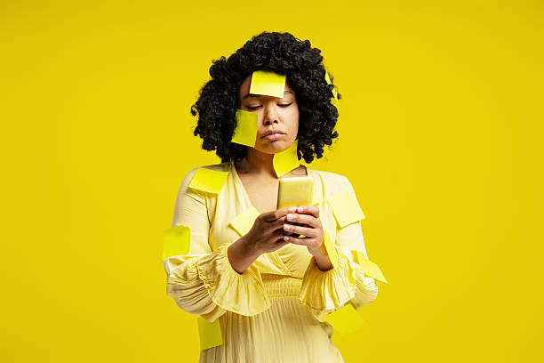 istock Young woman covered in yellow sticky notes using a smartphone on a yellow background 2218423485