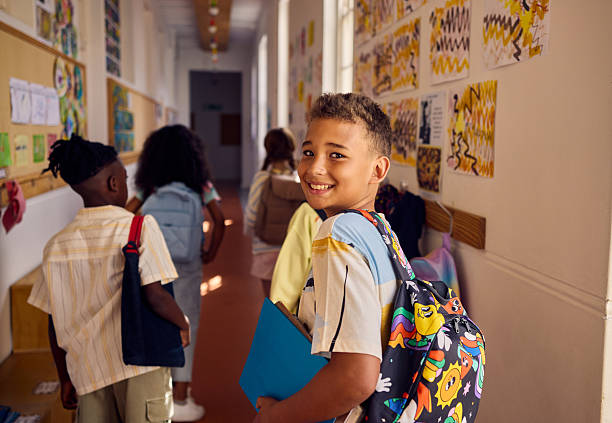 istock Smiling pupil walking down school hallway with backpack and book 2218430949