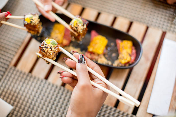 sushi on an exquisite white plate. Hands delicately hold chopsticks, preparing to savor each piece. The vibrant colors of the ingredients create an enticing look, It s the perfect moment to enjoy a delightful dish in a cozy setting