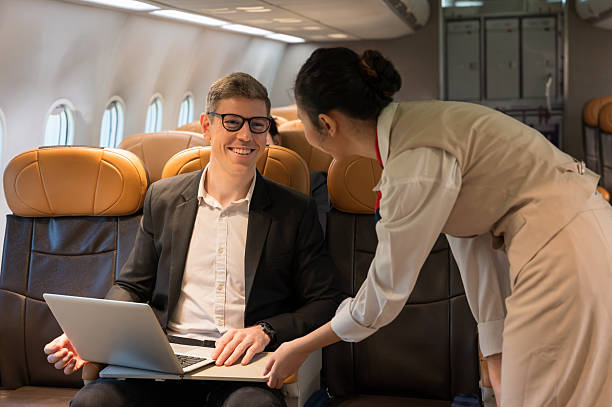 istock Smiling businessman working on laptop aboard airplane while friendly woman flight attendant provides service 2218433409