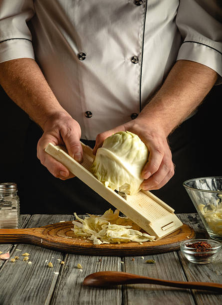 istock A chef skillfully slices a fresh cabbage with a mandoline on a wooden board in a warmly lit kitchen. Various kitchen tools adorn the countertop, creating a cozy culinary atmosphere 2218436058